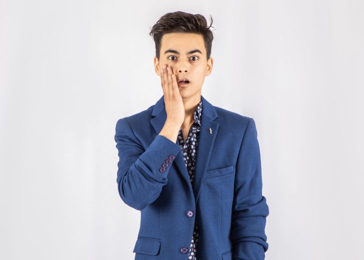 Photo of shocked man in blue blazer standing in front of white background