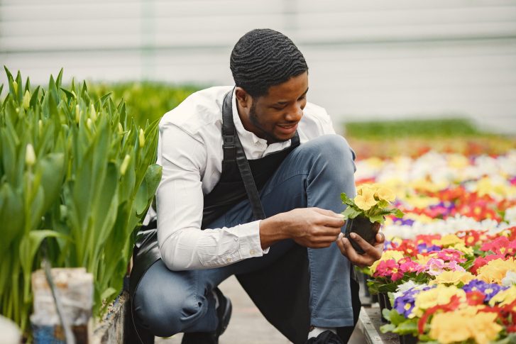 Gardner with elegant hairstyle crouching and holding a potted flower