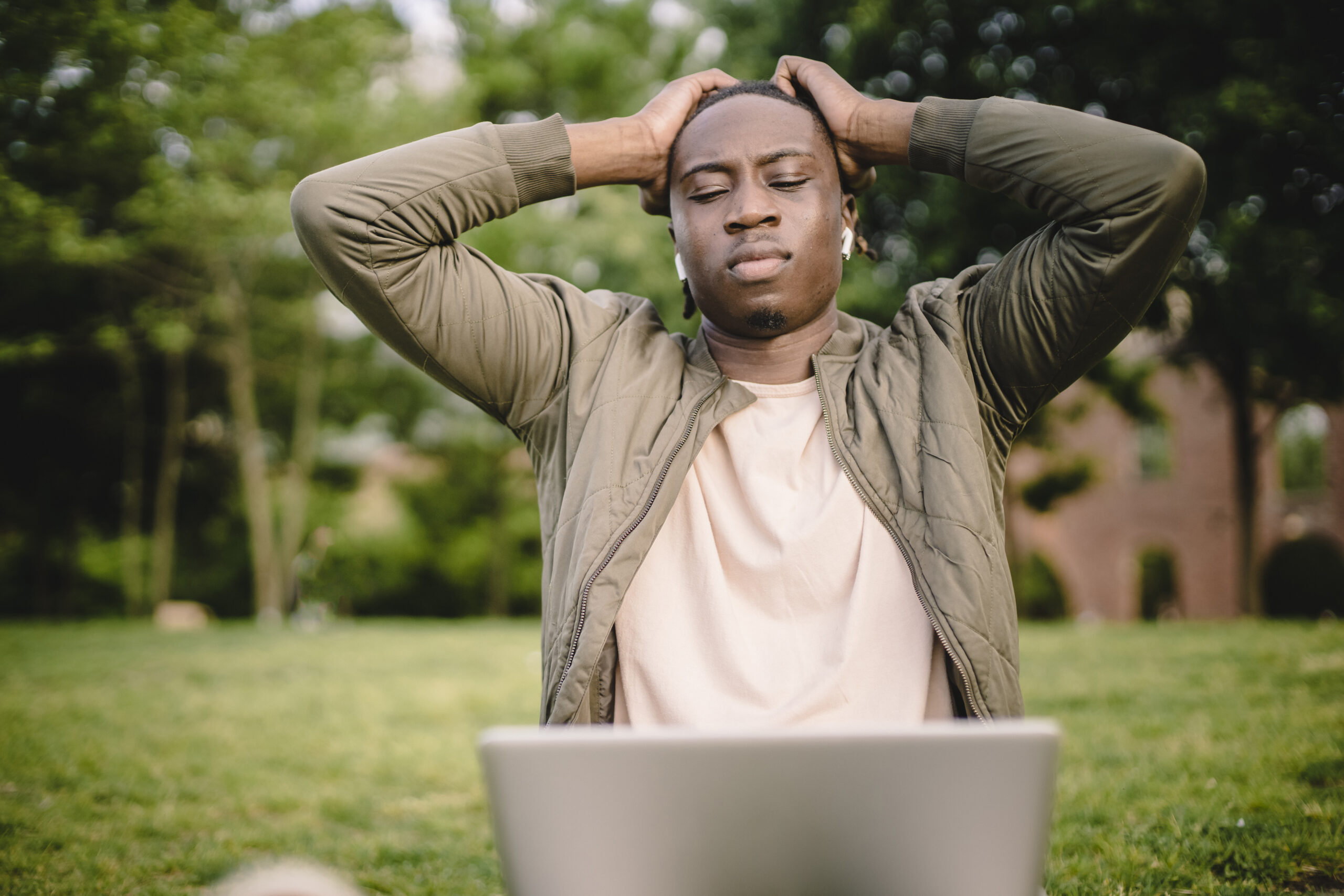 Upset ethnic man holding head reading information on laptop in park