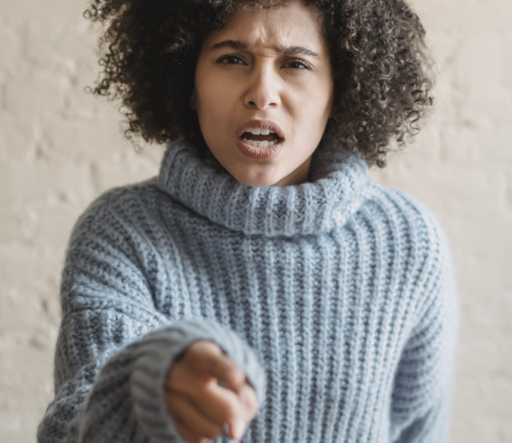 Unhappy ethnic woman pointing finger at camera in room